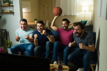 Excited male friends cheering while watching basketball game on tv at home