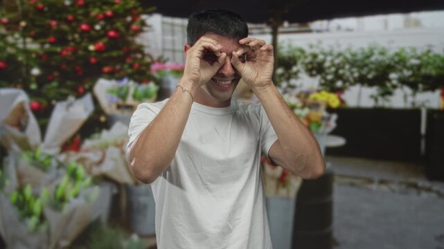 Man holds hands to eyes in binocular gesture at street flower shop with bouquet displayed on stall; curiosity.