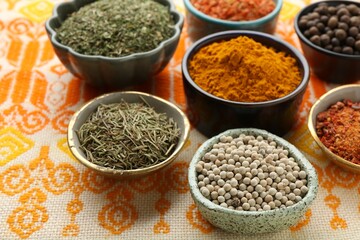 Many different aromatic spices in bowls on table with cloth, closeup
