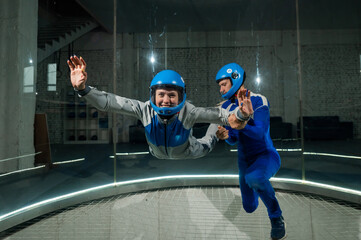 A male instructor teaches a woman how to fly in a wind tunnel. Free fall simulator.