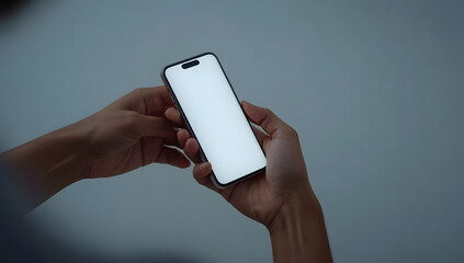 Close-up of hands holding a smartphone with a blank white screen against a neutral backdrop.