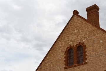 Large vintage prison made of stone. High roof pitch, red brick chimney. Barred windows.