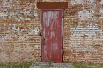 Very old metal door on prison compound. Red brick wall surrounding door.