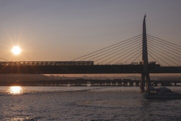Scenic sunset view of the Golden Horn Metro Bridge in Istanbul with warm sunlight, a passing boat, and shimmering water reflections, capturing the beauty and tranquility of the evening skyline.