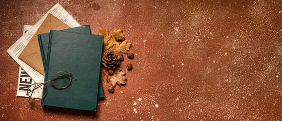 Stack of books, newspaper, envelope, eyeglasses and autumn decor on color background