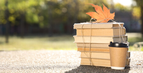 Stack of books, cup of coffee and autumn leaf on road in park