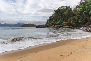 Ubatuba beach in São Paulo, with trees at the background, sand and waves.
Incredible paradisiac beach with cloudy sky.