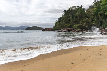 Ubatuba beach in São Paulo, with trees at the background, sand and waves.
Incredible paradisiac beach with cloudy sky.