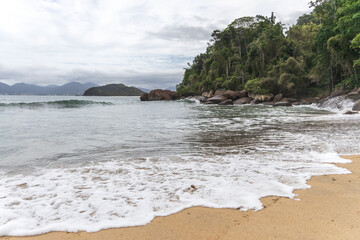 Ubatuba beach in São Paulo, with trees at the background, sand and waves.
Incredible paradisiac beach with cloudy sky.