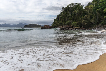 Ubatuba beach in São Paulo, with trees at the background, sand and waves.
Incredible paradisiac beach with cloudy sky.