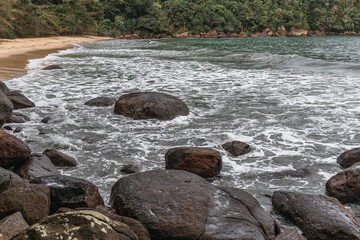 Ubatuba beach in São Paulo, with trees at the background, sand and waves.
Incredible paradisiac beach with cloudy sky.
