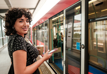 Young woman using smartphone and holding coffee at train station