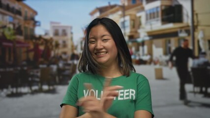 Young woman in green volunteer shirt smiling joyfully outdoors on a busy city street, embracing community spirit and engagement.
