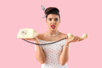 Displeased young pin-up woman with telephone on pink background