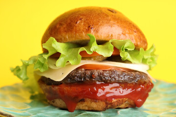 Plate with tasty burger on yellow background, closeup