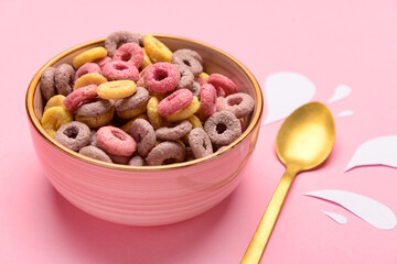 Bowl with colorful sweet cereal rings and paper milk drops on pink background