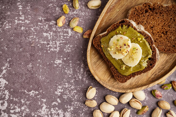 Wooden tray and pieces of bread with tasty pistachio paste on grey grunge background