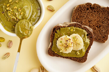 Bowl and pieces of bread with tasty pistachio paste on yellow background