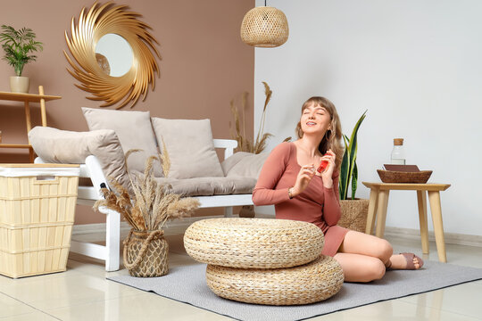 Young pretty woman sitting on floor with bottle of perfume in stylish living room - Powered by Adobe