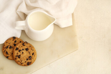 Board of sweet cookies with chocolate chips and jug of milk on white background