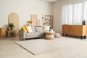 Interior of cozy living room with sofa, coffee table and shelving unit near white brick wall