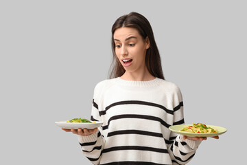 Surprised young woman with plates of tasty ravioli on grey background
