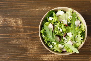 Bowl of healthy salad with radish on wooden background