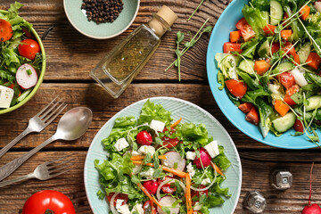 Bowls of fresh vegetable salad with radish and feta cheese on wooden background