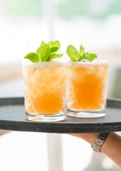 luxury orange tropical cocktails with mint garnish on waiter tray