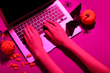 Female hands with  modern laptop, candy corns and decorations for Halloween on color background, closeup