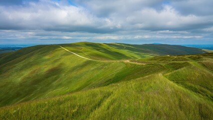 Obraz premium A scenic view of grassy hills under a cloudy sky with a visible path winding through the landscape