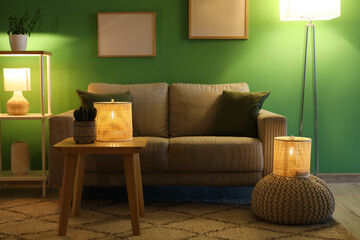 Cozy sofa, coffee table and pouf with glowing lamps in interior of living room