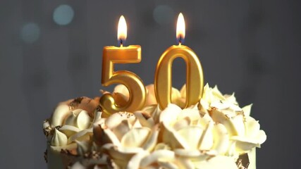 Close-up of a beautifully decorated 50th birthday cake with golden number candles '5' and '0' lit on top, soft bokeh lights in the background