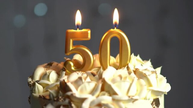 Close-up of a beautifully decorated 50th birthday cake with golden number candles '5' and '0' lit on top, soft bokeh lights in the background - Powered by Adobe