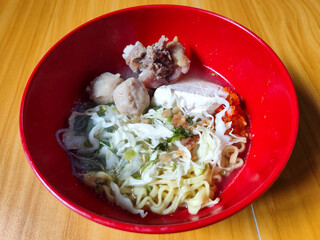 Bakso. The meatballs are served in a red bowl, containing meatballs, pieces of beef bone, yellow vermicelli noodles, vegetables, etc. Looks very delicious and delicious.