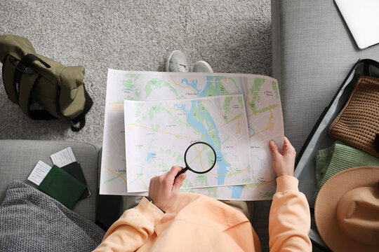 Young male tourist with map, backpack and magnifying glass planning his trip at home, top view. Itinerary concept