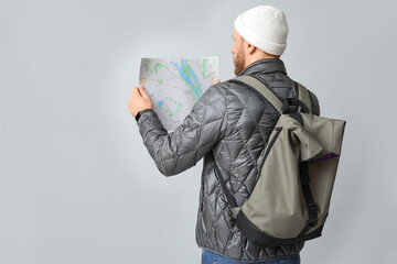 Young male tourist with backpack looking at map on grey background, back view. Itinerary concept