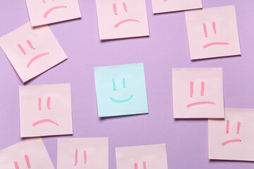 Sticky note with happy face amongst sad faces on lilac background