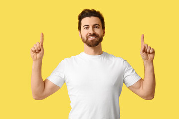 Fototapeta premium Young man pointing up on yellow background