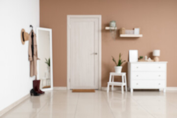 Blurred view of stylish hallway with mirror, chest of drawers and white door