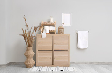 Interior of stylish restroom with wooden cabinet, towel and rolls of toilet paper