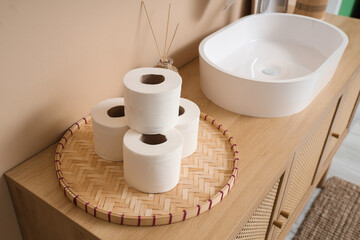 Wicker mat with rolls of toilet paper on wooden cabinet in bathroom, closeup