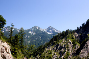 Obraz premium Majestic mountain range rises under a clear blue sky in a stunning natural landscape surrounded by lush green trees