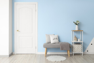 Interior of stylish hallway with grey bench, shelving unit and white door