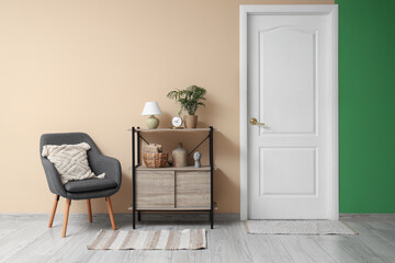 Interior of stylish hallway with grey armchair, shelving unit and white door
