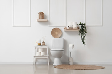 Interior of stylish restroom with toilet bowl, decor and rolls of toilet paper