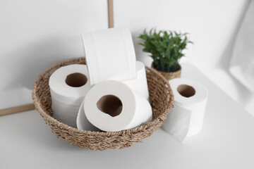 Wicker basket with rolls of toilet paper on chest of drawers near white brick wall, closeup