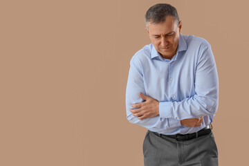 Mature businessman suffering from bellyache on beige background