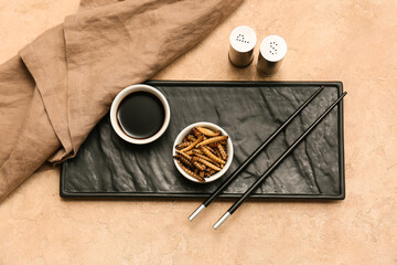 Bowl with fried maggots and soy sauce on beige background