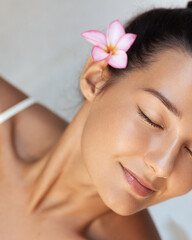 Fototapeta premium Serene Woman With Flower In Hair Relaxing With Glowing Skin At Spa